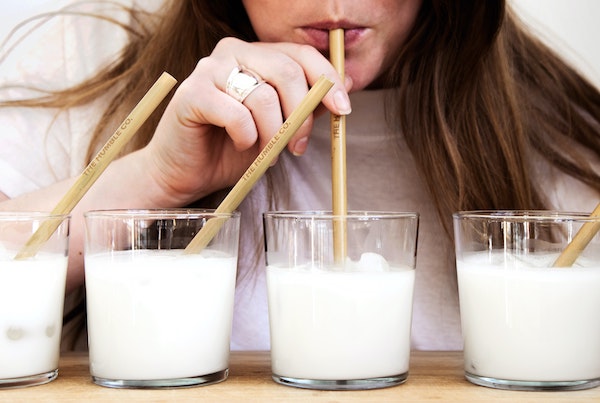 a girl drinking milk from a glass with a wooden straw